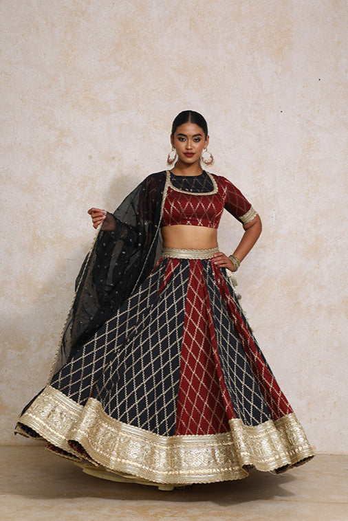 Woman wearing a traditional red and black lehenga with gold accents on a beige background