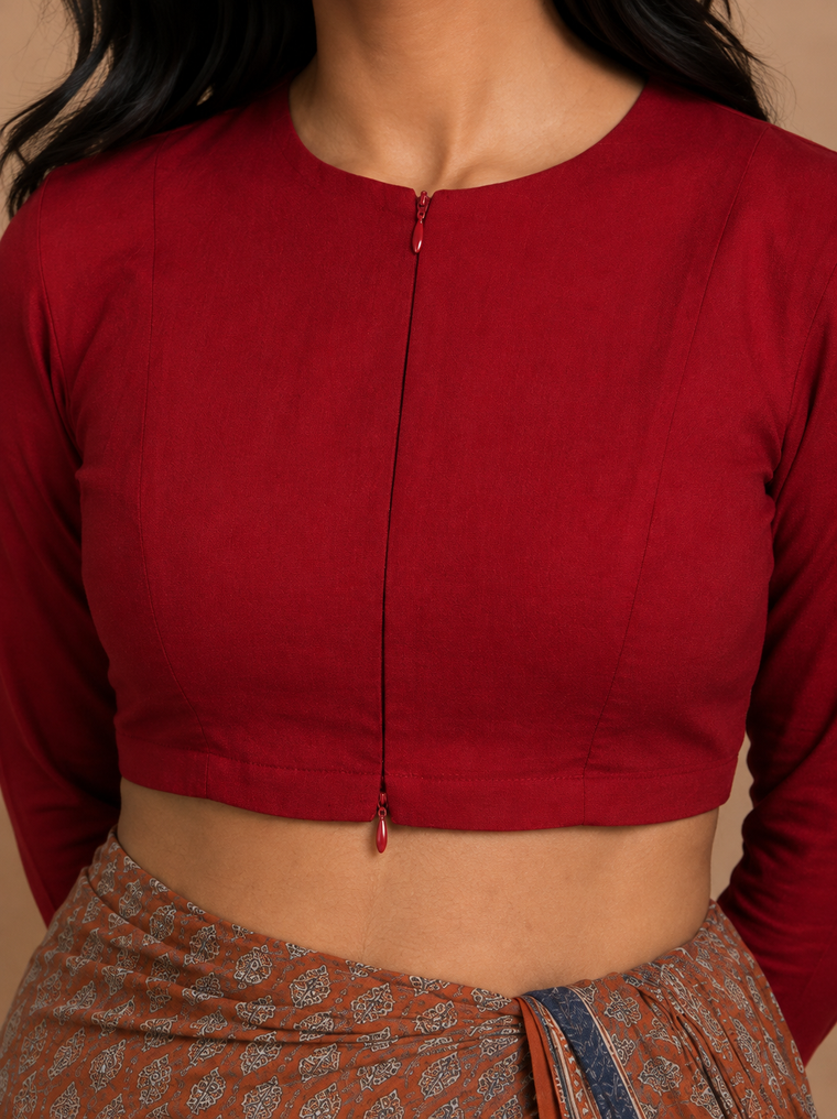 A close-up of a model wearing a long-sleeve red crop top with a front zipper and a patterned rust-orange skirt.